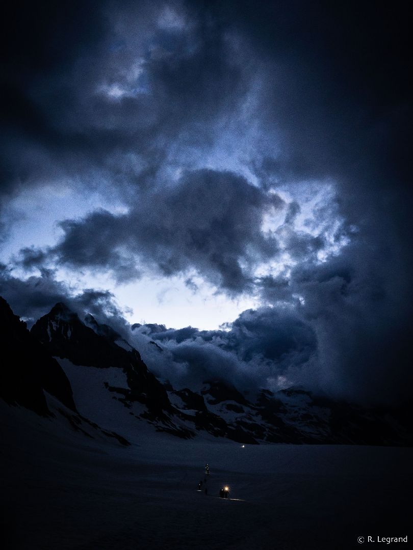 Des alpinistes traversent une étendue de neige avec leur frontale à l'aube